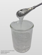 Versagel ME 750 semisolid gelled lip gloss base is shown dripping from a metal spoon into a glass beaker against a light gray background. Small text in the lower-left corner reads 'Viscosity @ 25°C (ASTM D2983) 85,000-110,000 cPs Mineral oil-free'.