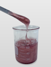 A sample of red DIY lip gloss made with Versagel ME 750 drips own from a spatula into a glass beaker.